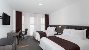 Habitación de hotel con dos camas, un escritorio, una silla, un televisor y una ventana con cortinas.