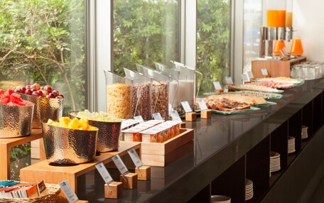 A buffet with various food items and a view of greenery outside.