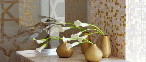 Tres jarrones dorados con flores blancas sobre una encimera de baño.