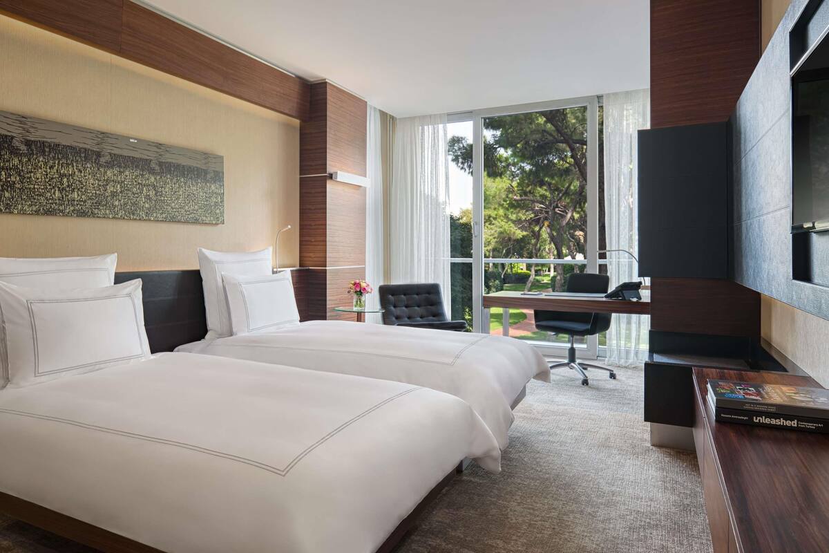 Une chambre d’hôtel avec un grand lit, un bureau, une chaise, une télévision et une vue sur l’extérieur.