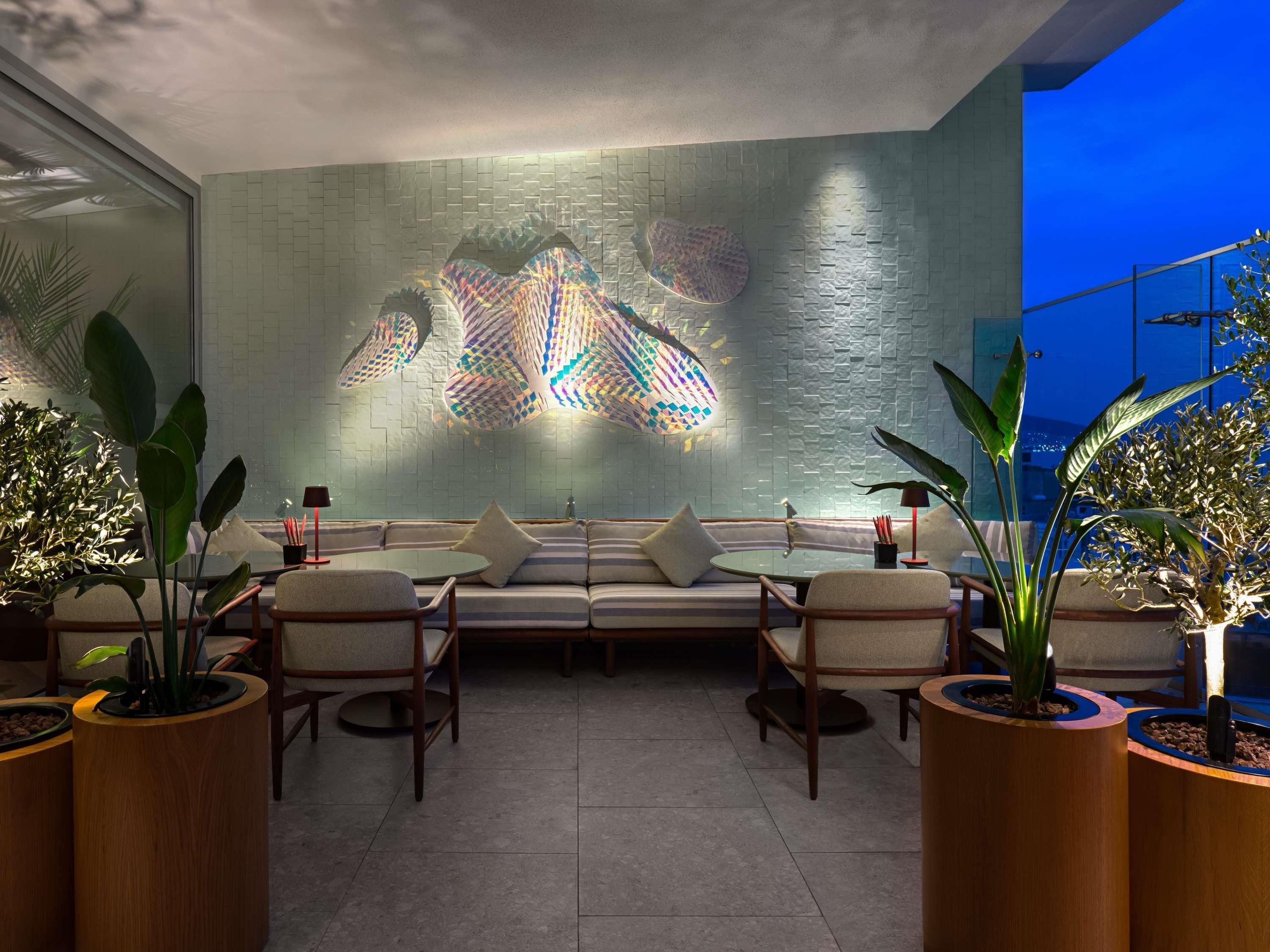 A modern lounge area with a sofa, chairs, and a table, featuring a textured wall and potted plants.