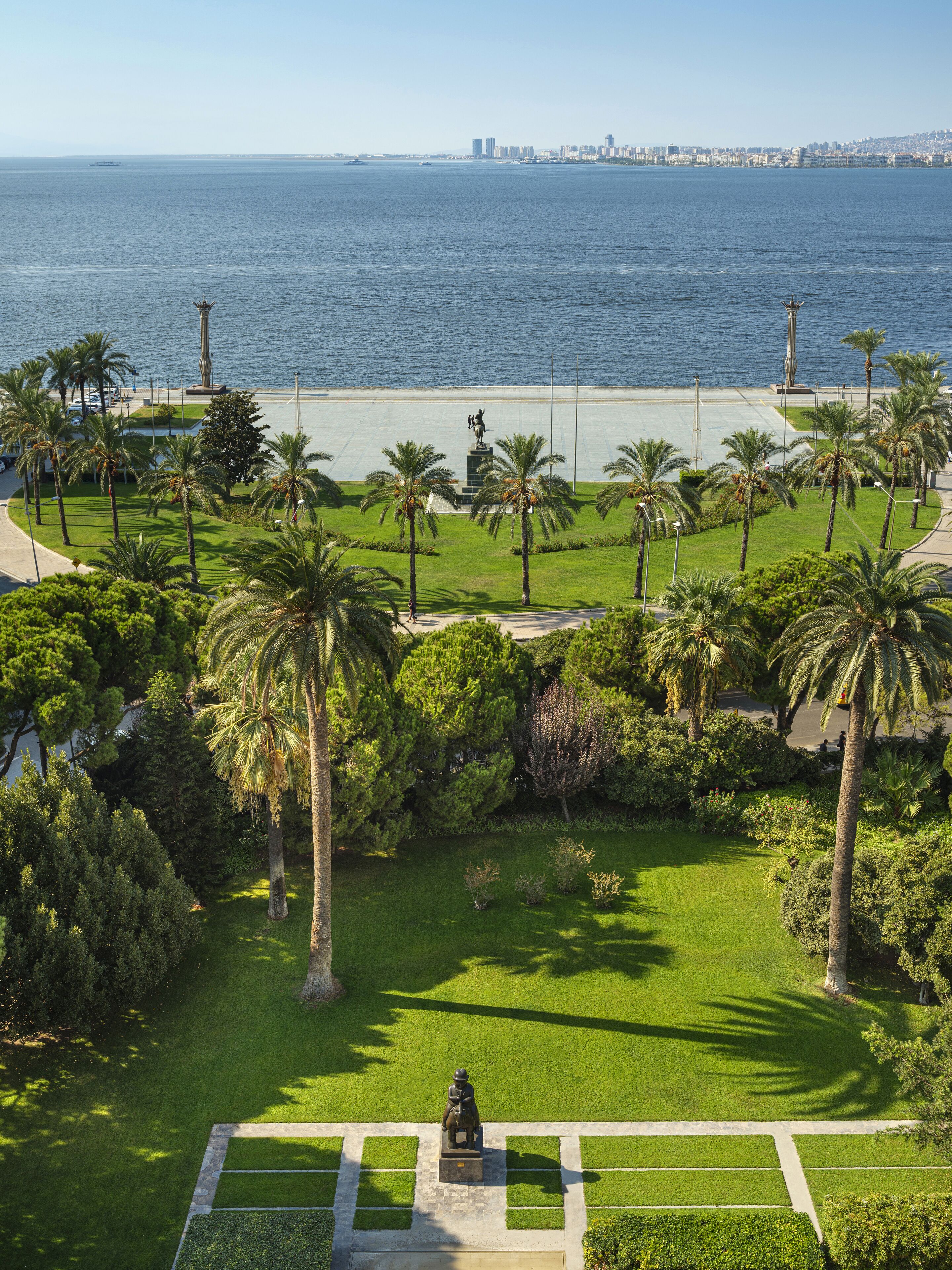 Un parc avec une statue, des palmiers et une vue sur la mer.
