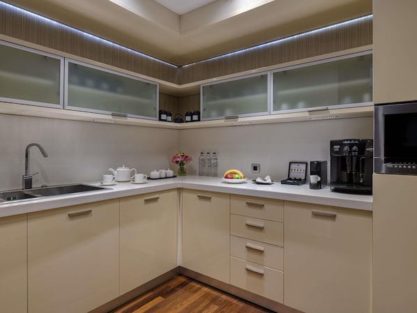 Una cocina moderna con un lavaplatos de acero inoxidable, armarios blancos, una cafetera y un microondas.