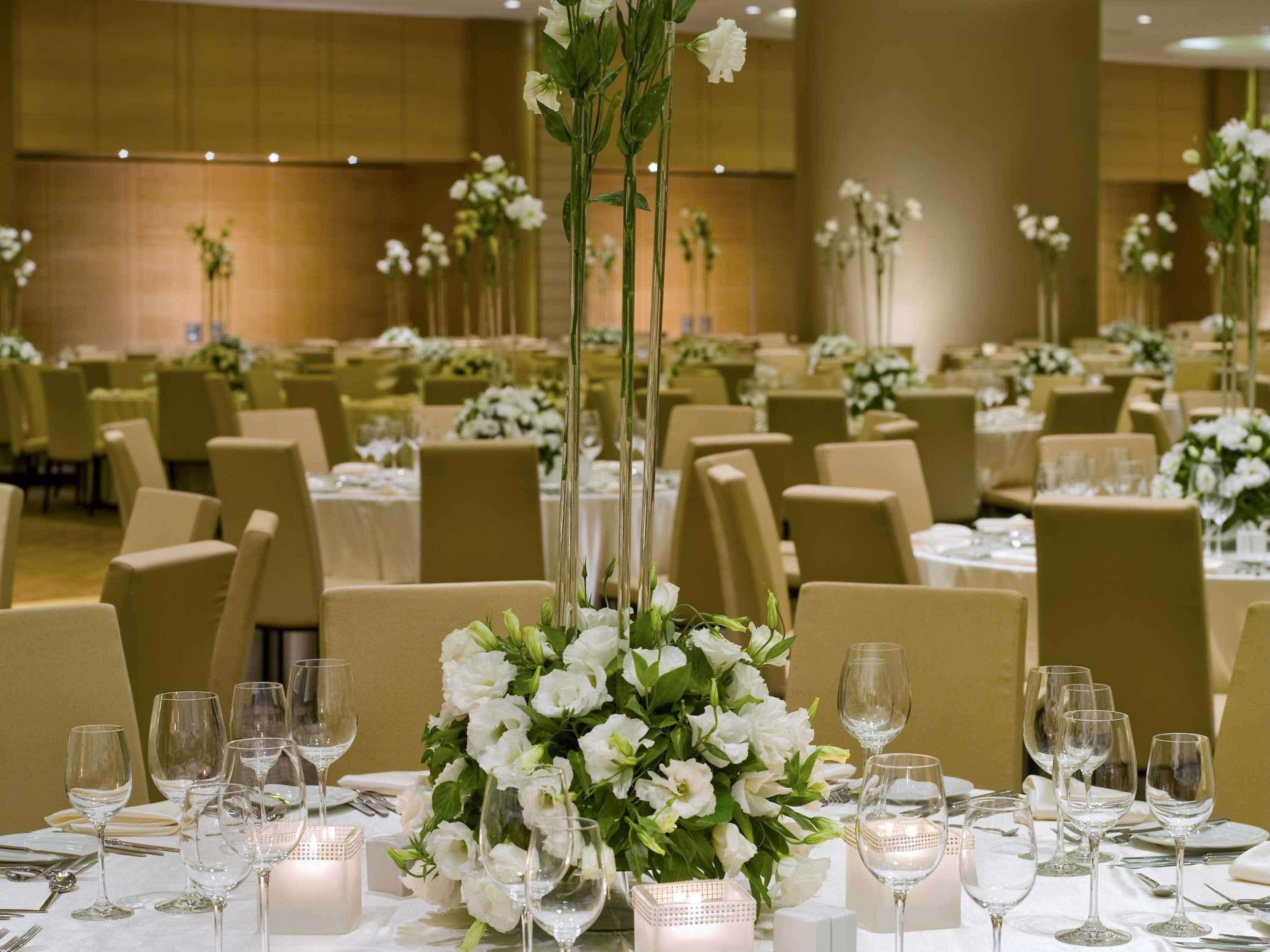 Un salón de banquetes con mesas redondas, sillas y centros de mesa con flores.
