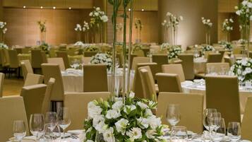 Un salón de banquetes con mesas redondas, sillas y centros de mesa con flores.