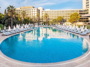 Una piscina amplia i cristal·lina envoltada de gandules i ombrel·les, amb edificis moderns al fons.