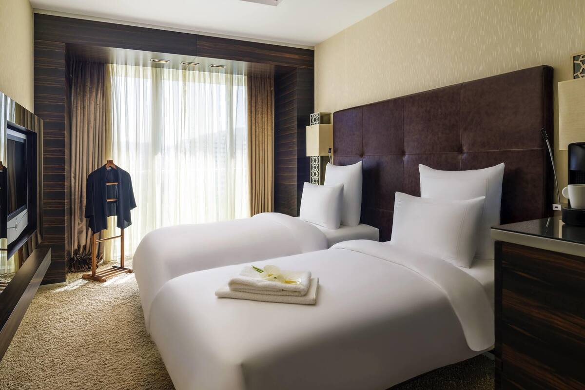 Ein Hotelzimmer mit zwei Betten, einem Fernseher, einem Schreibtisch und einem Fenster mit Vorhängen.