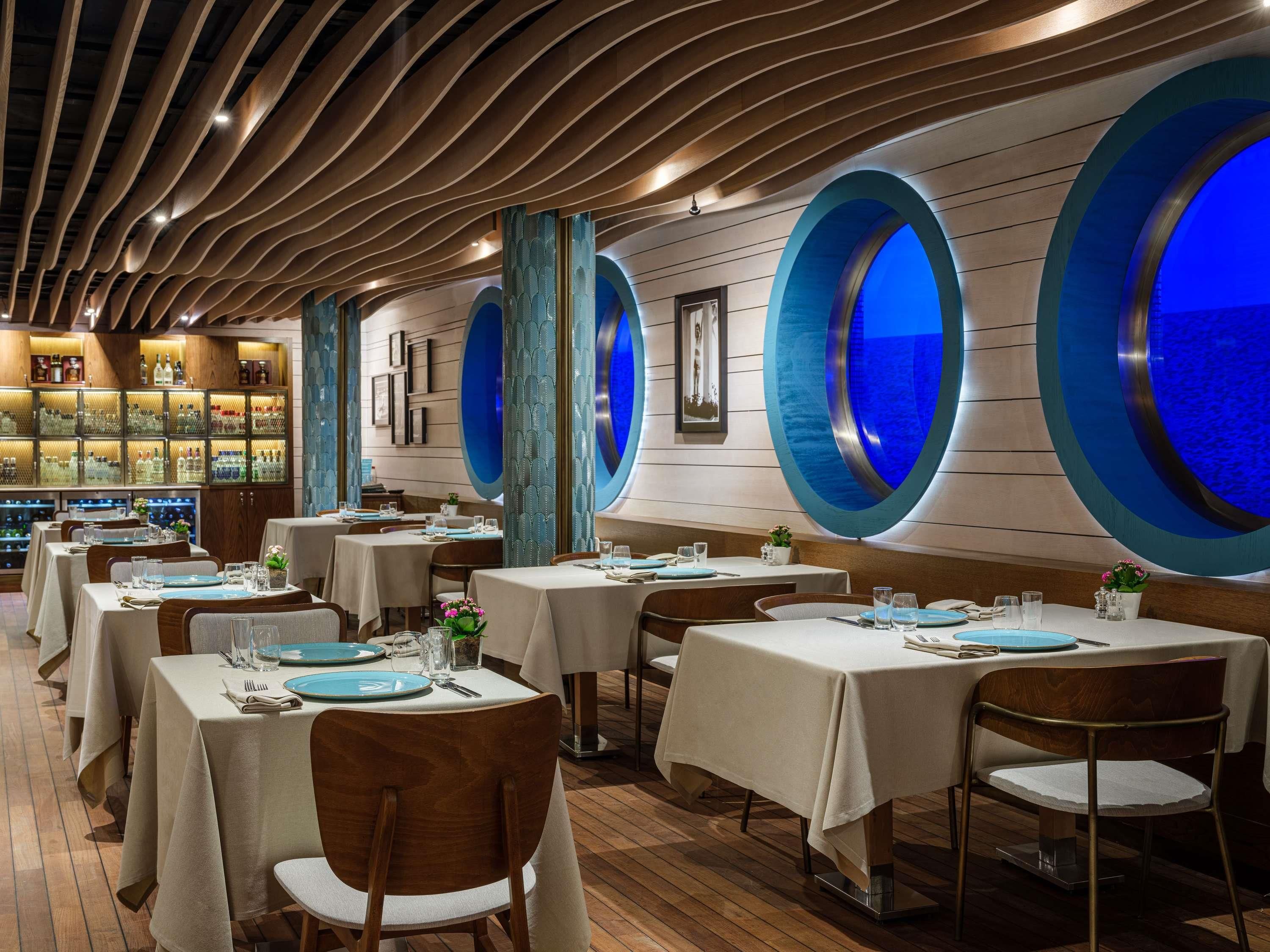 A restaurant with round blue windows, wooden ceiling, and tables set for dining.