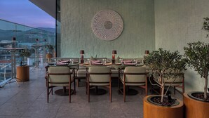 Un'area pranzo con un tavolo apparecchiato per sei persone, circondato da sedie, decorata con un elemento decorativo sopra e piante in vaso su entrambi i lati.