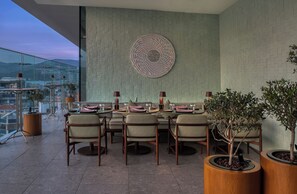 A dining area with a table set for six, surrounded by chairs, with a decorative wall piece above and potted plants on either side. - Swissotel Buyuk Efes Izmir (Izmir)