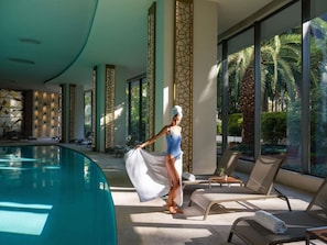 Un espace aménagé au bord de la piscine, avec des chaises longues, une piscine et de grandes fenêtres offrant une vue sur les palmiers.