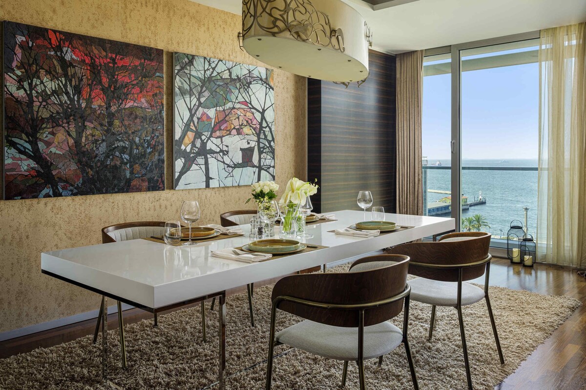Un coin repas avec une table blanche, des chaises marron et un grand tableau accroché au mur.