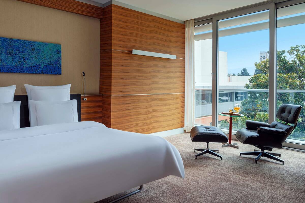 Une chambre d’hôtel moderne dotée d’un grand lit, d’un mur décoratif en bois, d’une grande fenêtre donnant sur la ville et d’une petite table avec une chaise.