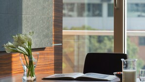Un ufficio moderno con una scrivania in legno, un vaso in vetro trasparente con fiori bianchi, un libro aperto, una caraffa di vetro con latte e una sedia nera.