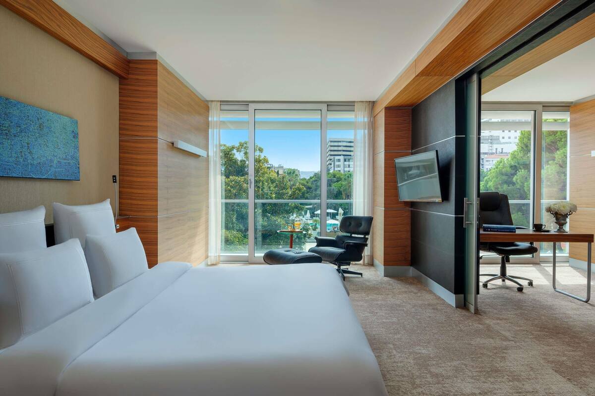 Une chambre d’hôtel avec un grand lit, un bureau avec une chaise, une télévision et une vue sur l’extérieur.
