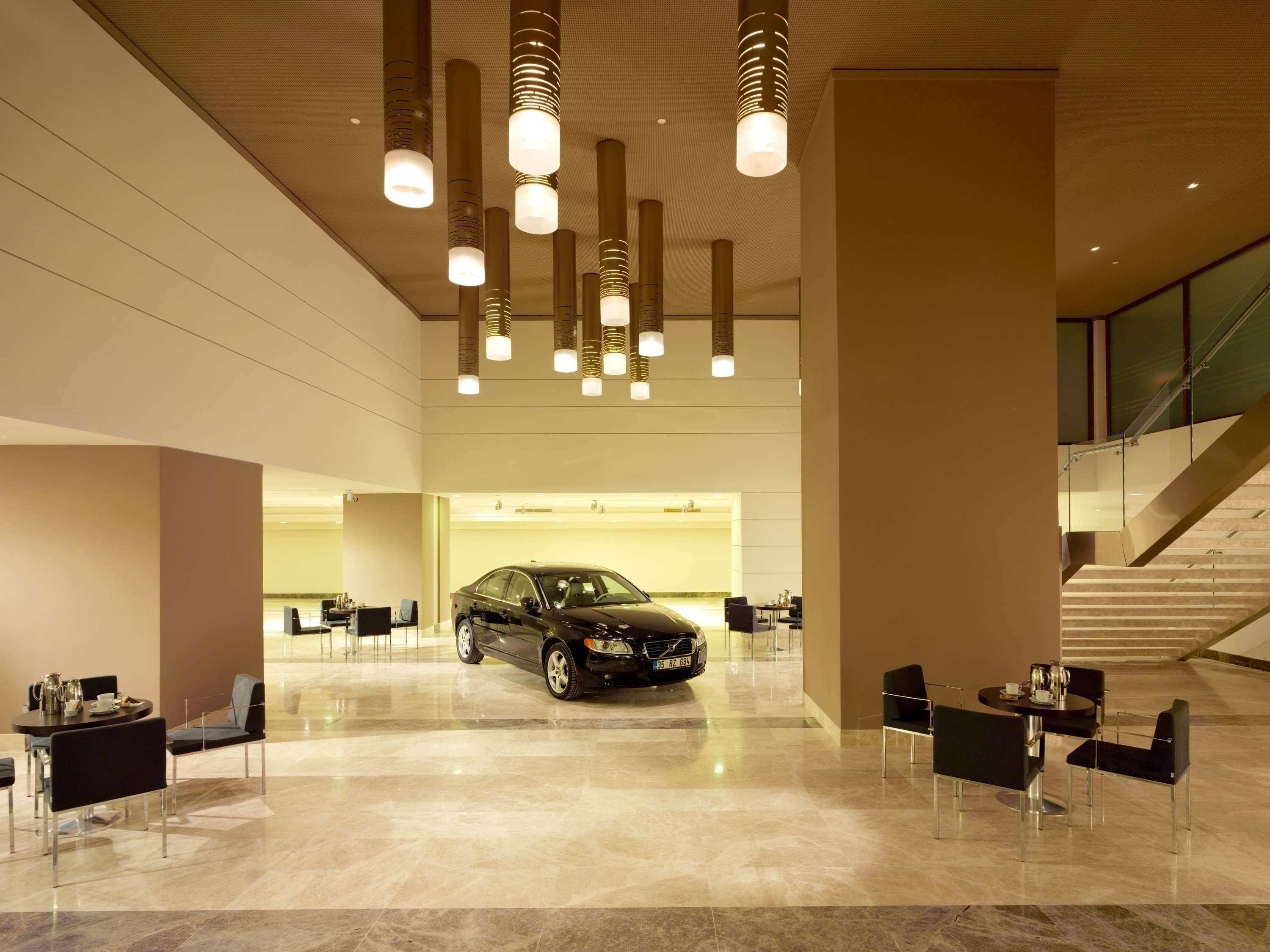 A spacious lobby with a car parked in the center, modern pendant lighting, and a staircase in the background.
