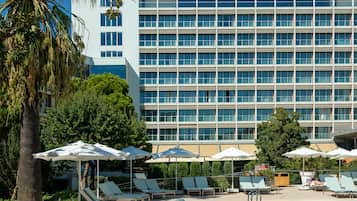 Un hotel con zona de piscina, tumbonas, sombrillas y un cielo azul despejado.