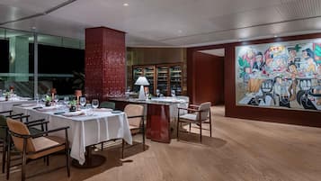 A dining area with tables set for multiple guests, a large mural on the wall, and a wine rack in the background.