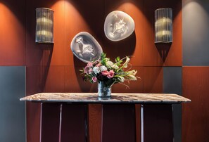 Un mostrador de recepción con un jarrón de flores, dos lámparas de pared y un panel decorativo.
