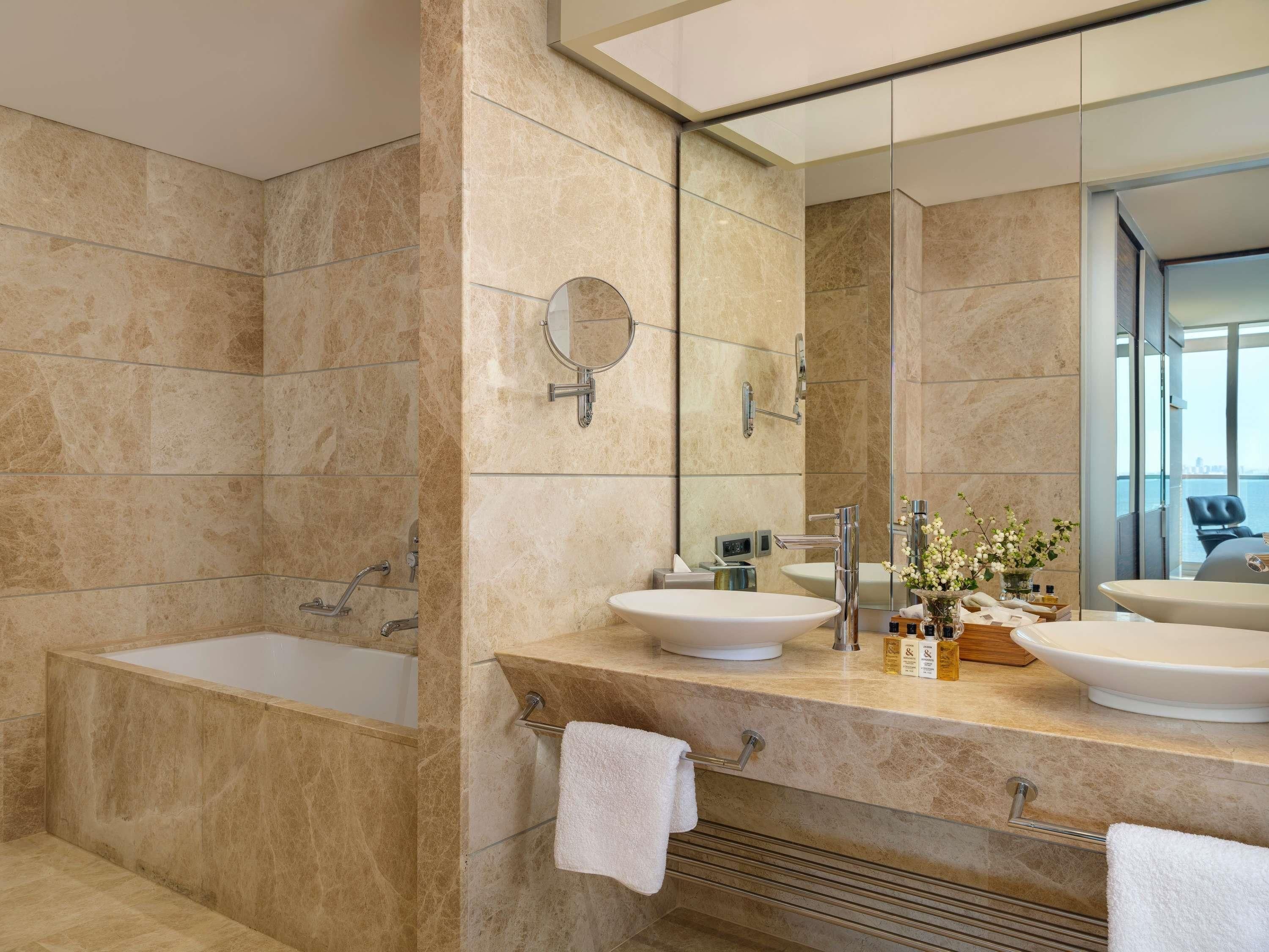 Un baño moderno con bañera, dos lavamanos, un espejo grande y vistas a la ciudad.