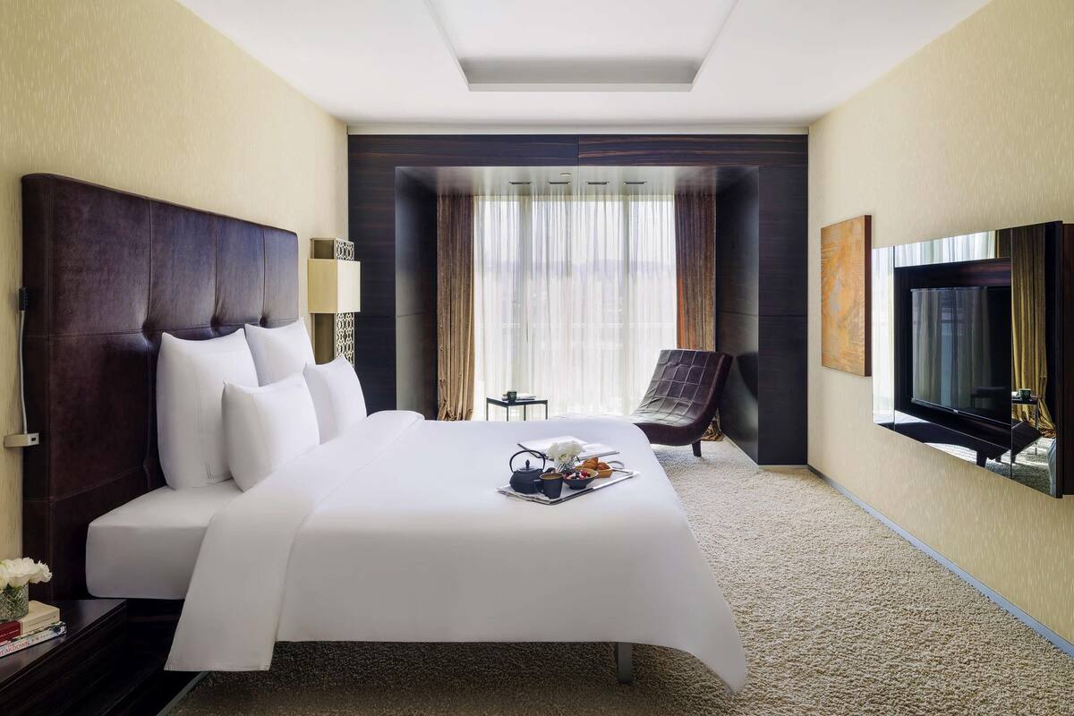Habitación de hotel con una cama grande, televisión, una silla y una mesita con una bandeja de objetos.