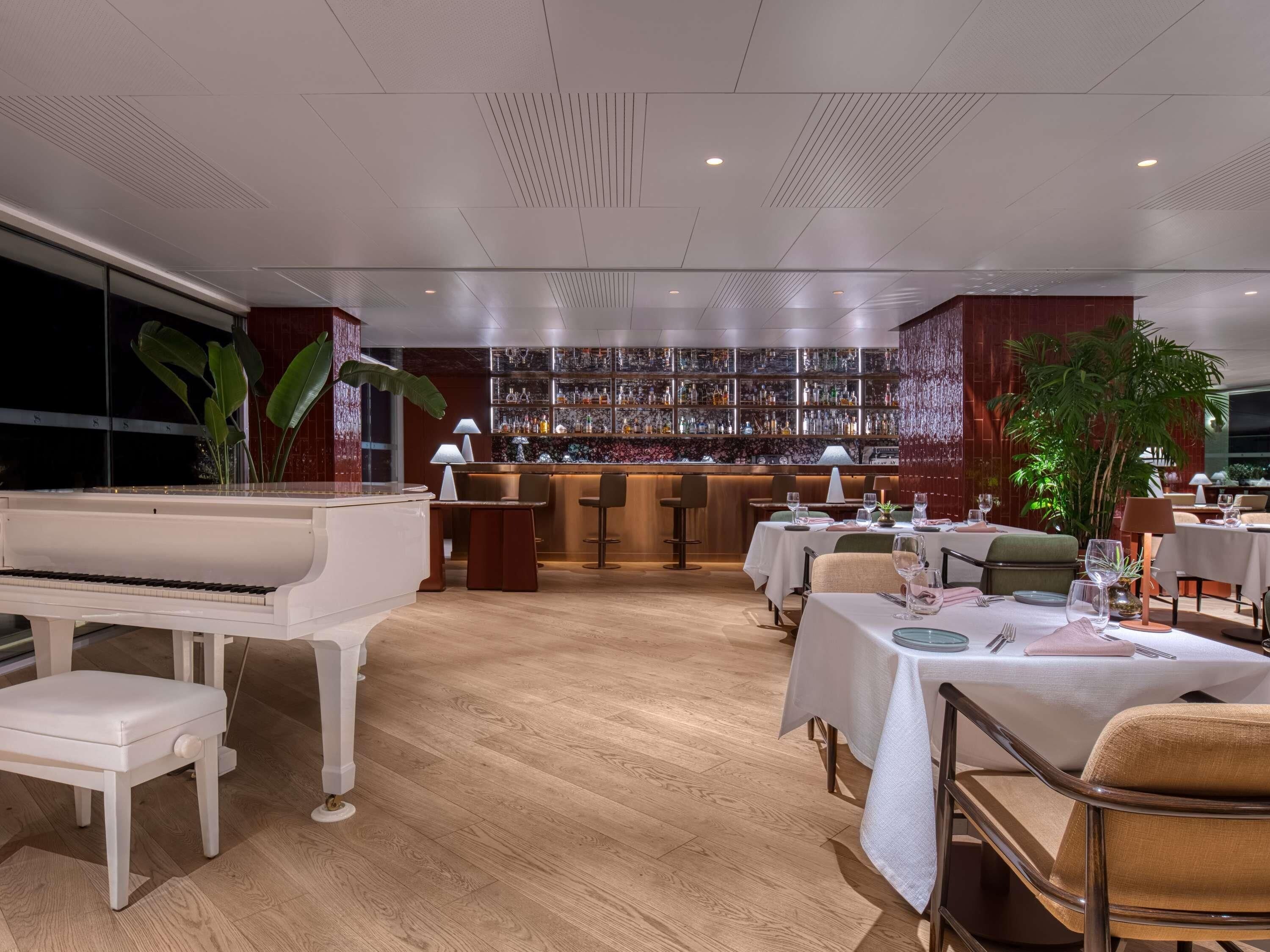 Un restaurante con piano, zona de bar y mesas para comer.