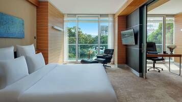 A hotel room with a large bed, a desk with a chair, a TV, and a view of the outdoors.