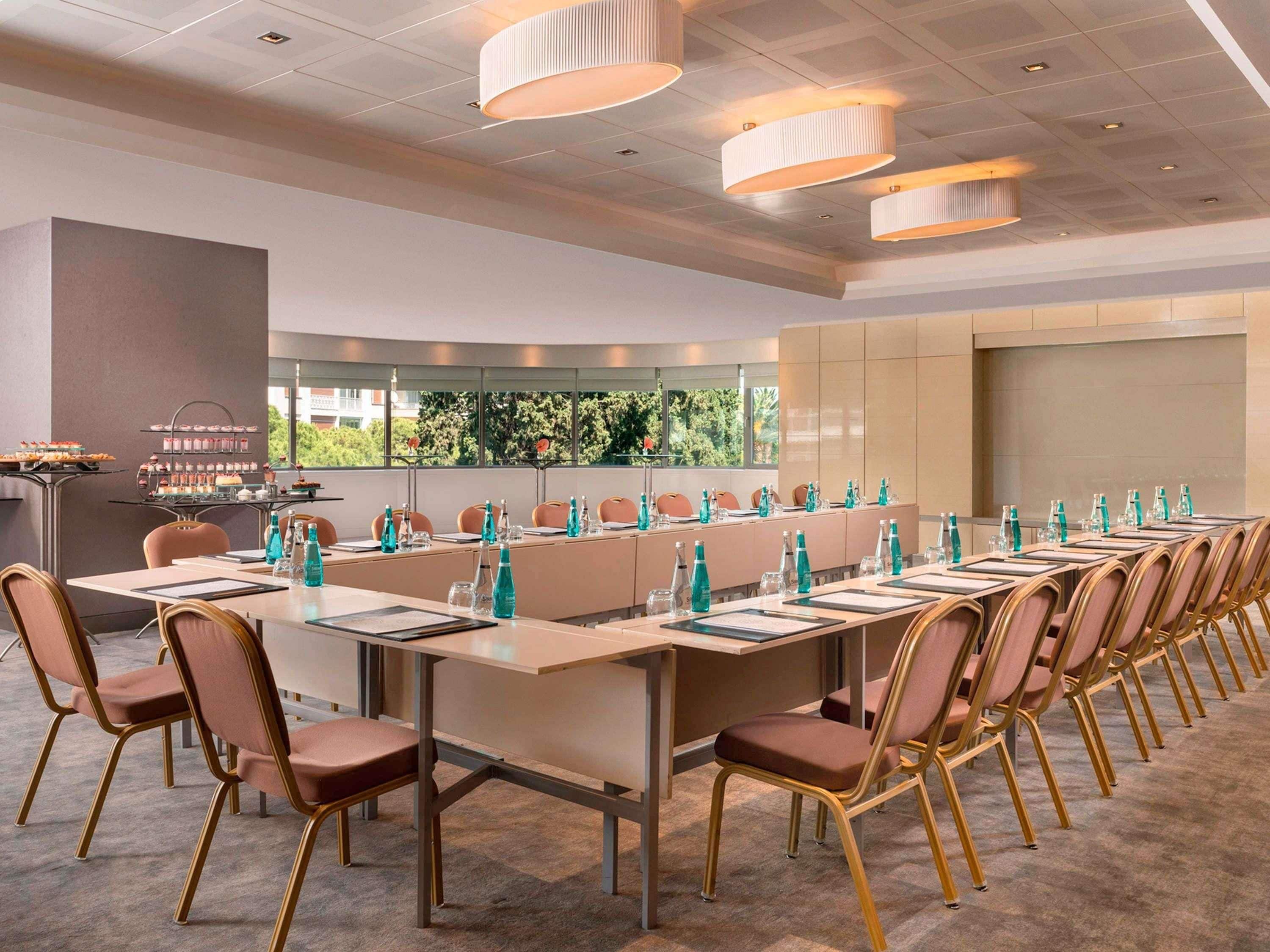 A conference room with long tables, chairs, and a buffet area with desserts.