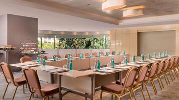 A conference room with long tables, chairs, and a buffet area with desserts.