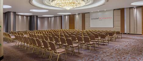 A conference room with rows of chairs, a large chandelier, and a screen displaying 'swissotel BUYUKIFESES IZMIR'.