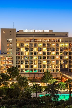 A hotel with a modern facade, multiple floors, and a swimming pool area.