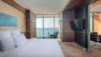 A modern hotel room with a large bed, a seating area with a view, and a flat-screen TV mounted on the wall.