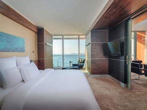 Una habitación de hotel moderna con una cama grande, una zona de estar con vistas y un televisor de pantalla plana en la pared.