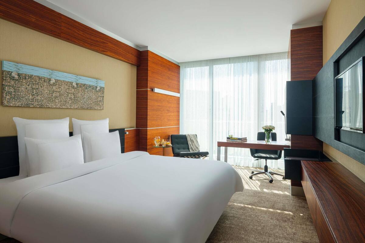Une chambre d’hôtel avec un grand lit, un bureau, une chaise, une télévision et une fenêtre avec des rideaux.