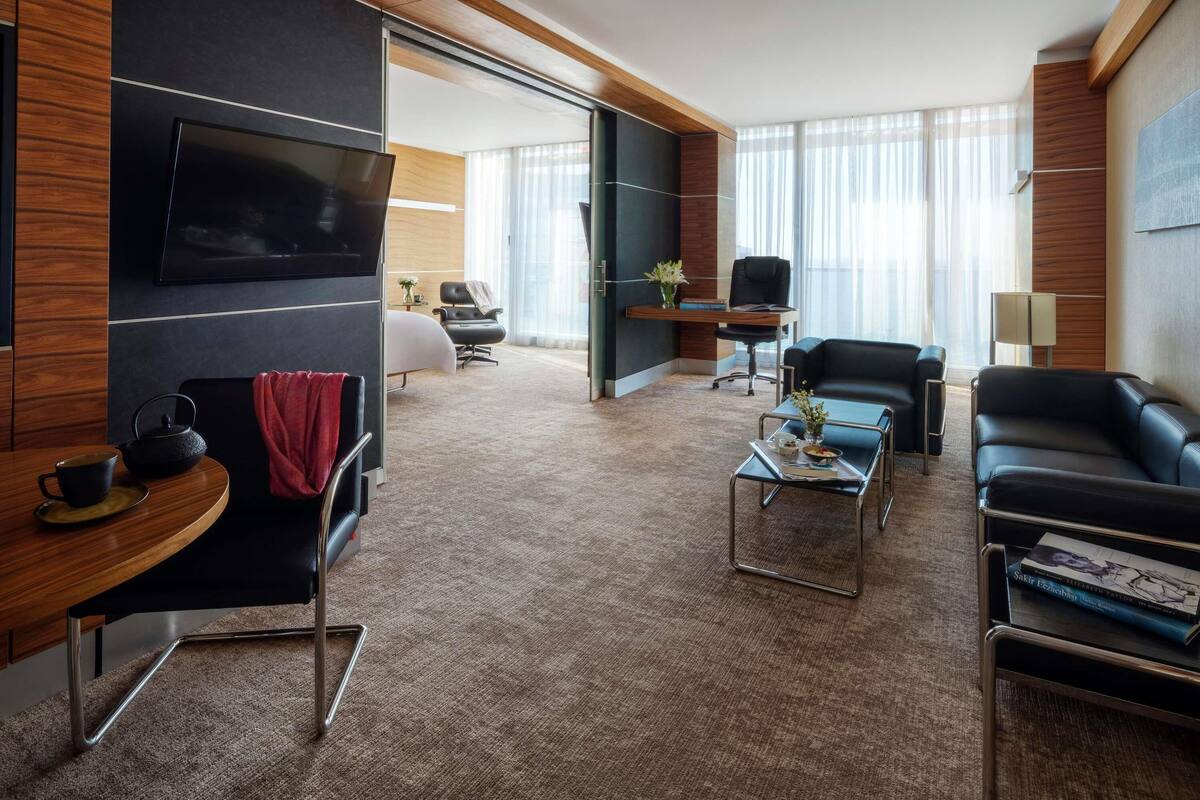 Ein modernes Hotelzimmer mit Flachbildfernseher, Ledersitzgelegenheiten, einem Couchtisch und einem Schreibtisch mit Stuhl.