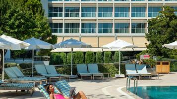 A poolside area with lounge chairs, umbrellas, and a building in the background.