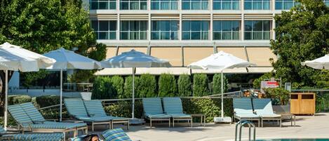 A poolside area with lounge chairs, umbrellas, and a building in the background.