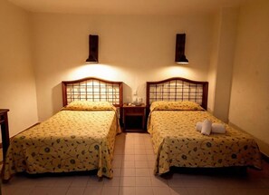 Een kamer met twee enkele bedden, elk met een houten hoofdbord en een bedspread met bloemenprint. Tussen de bedden staat een nachtkastje met een lamp en een klein tafeltje.