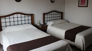 Dos camas individuales con cabeceros de madera, una mesita de noche con un teléfono y un cuadro en la pared.