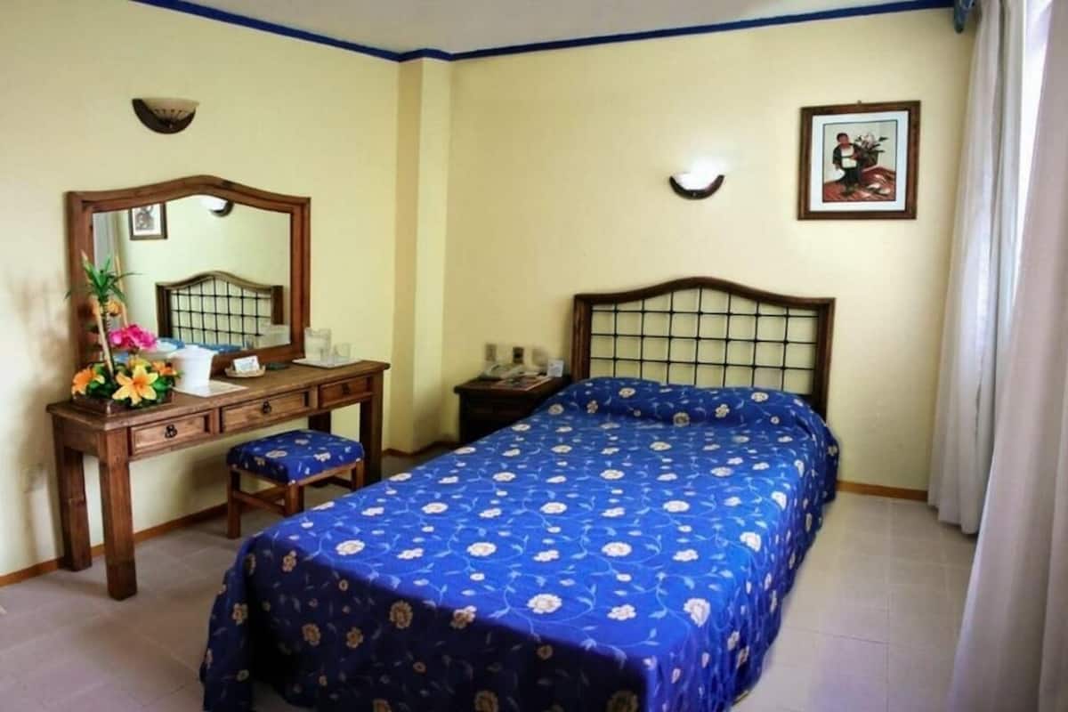 Een slaapkamer met een bed, een dressoir, een spiegel en een nachtkastje.