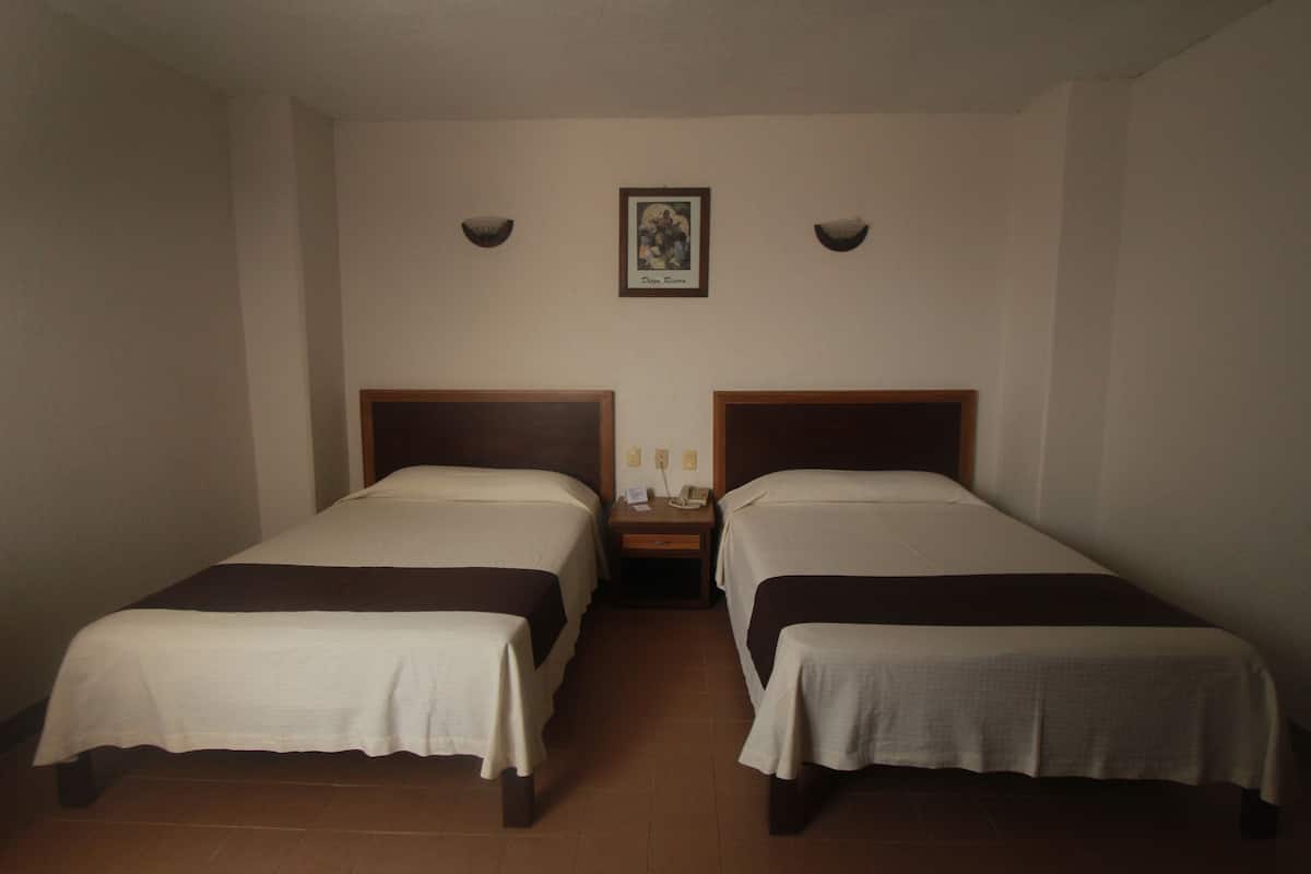 Een hotelkamer met twee enkele bedden, een nachtkastje met een telefoon en een lijst op de muur.