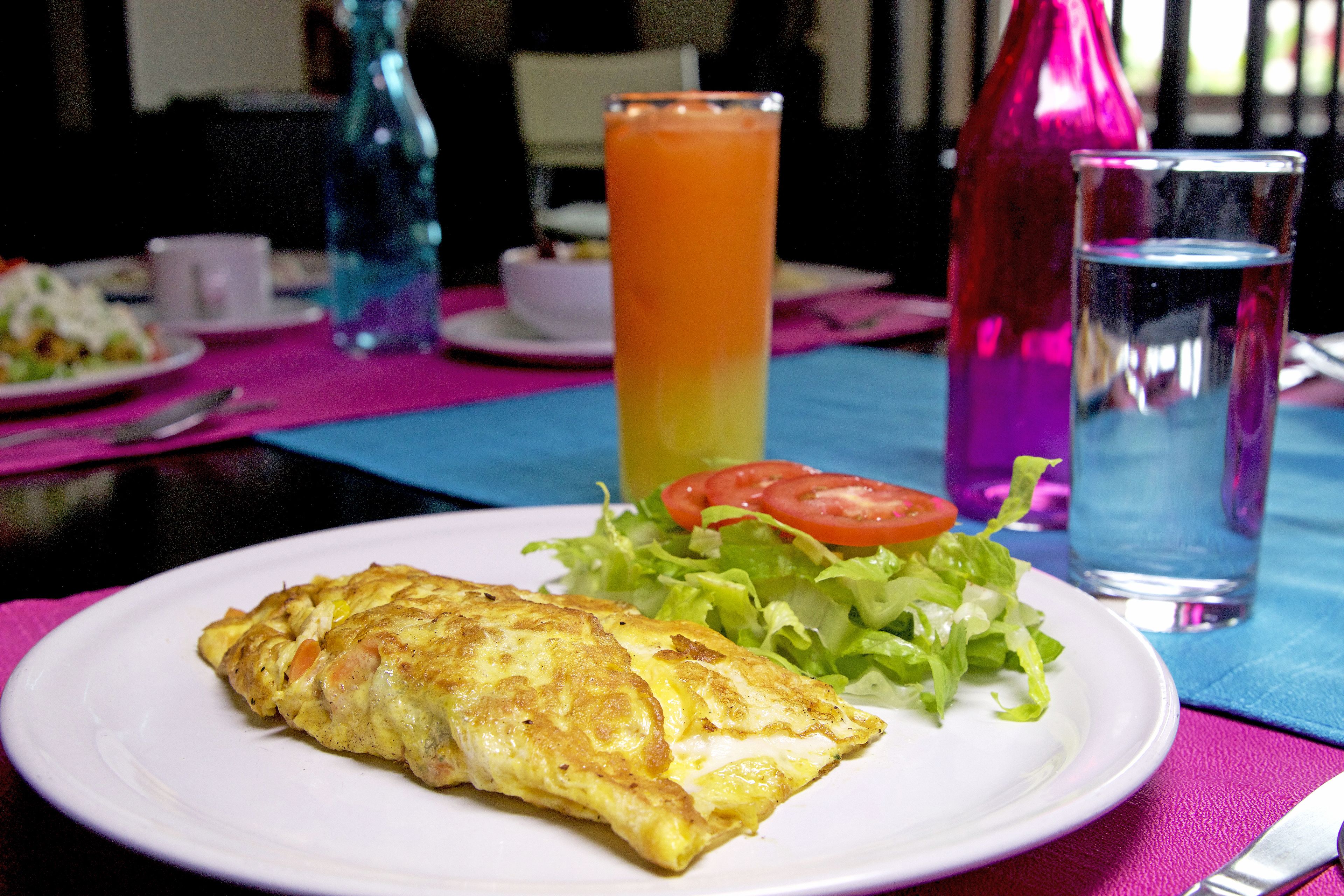 Un piatto con un'omelette, una fetta di pomodoro e lattuga su un tavolo con una tovaglia rosa.