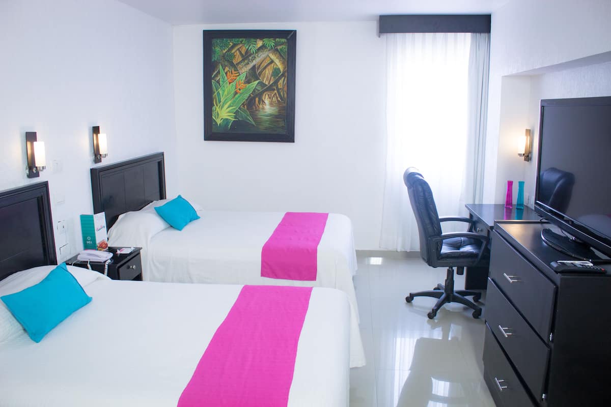 A hotel room with two beds, a desk, a chair, a TV, and a painting on the wall.