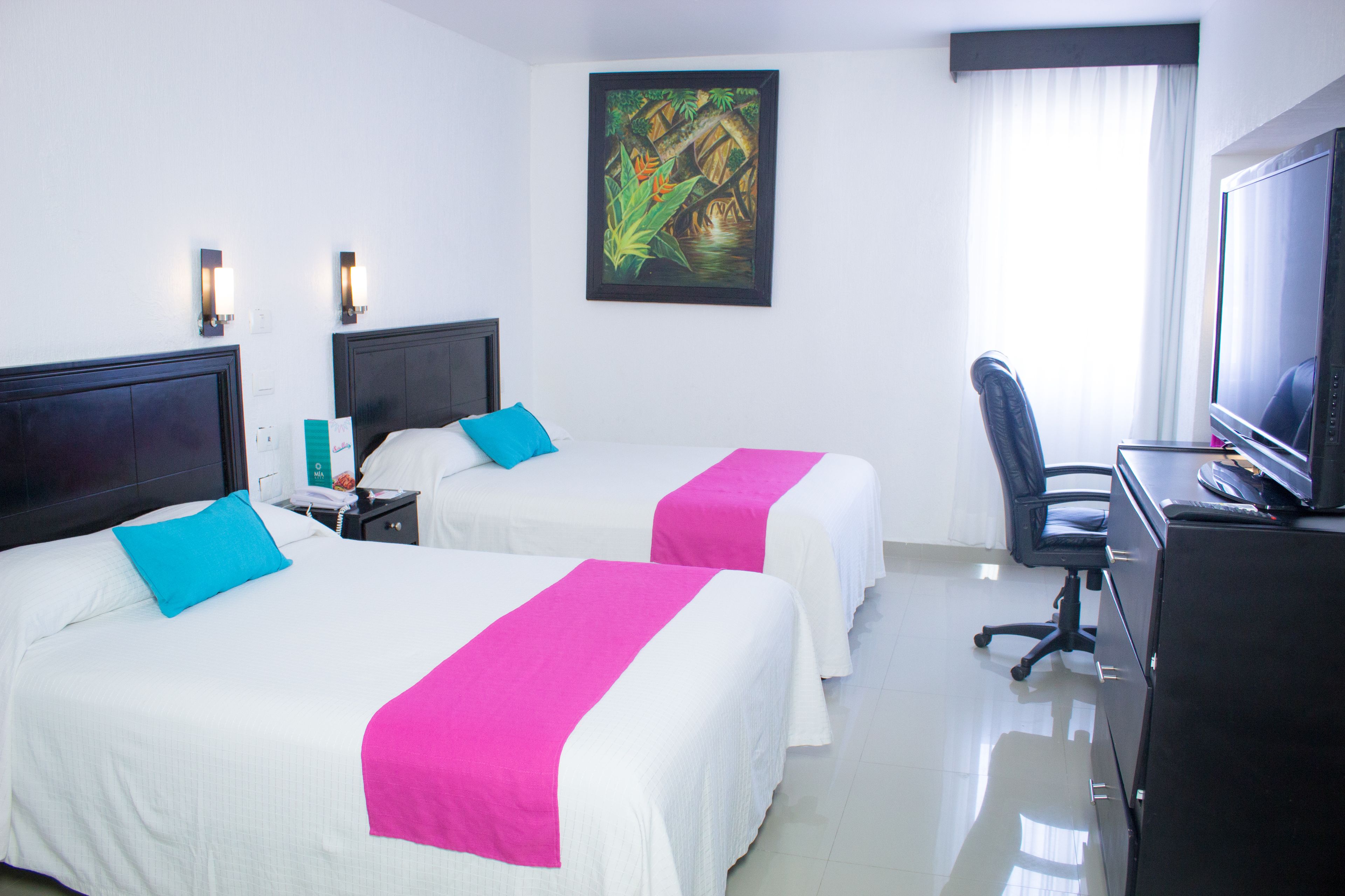A hotel room with two beds, a desk with a computer, a TV, and a painting on the wall.