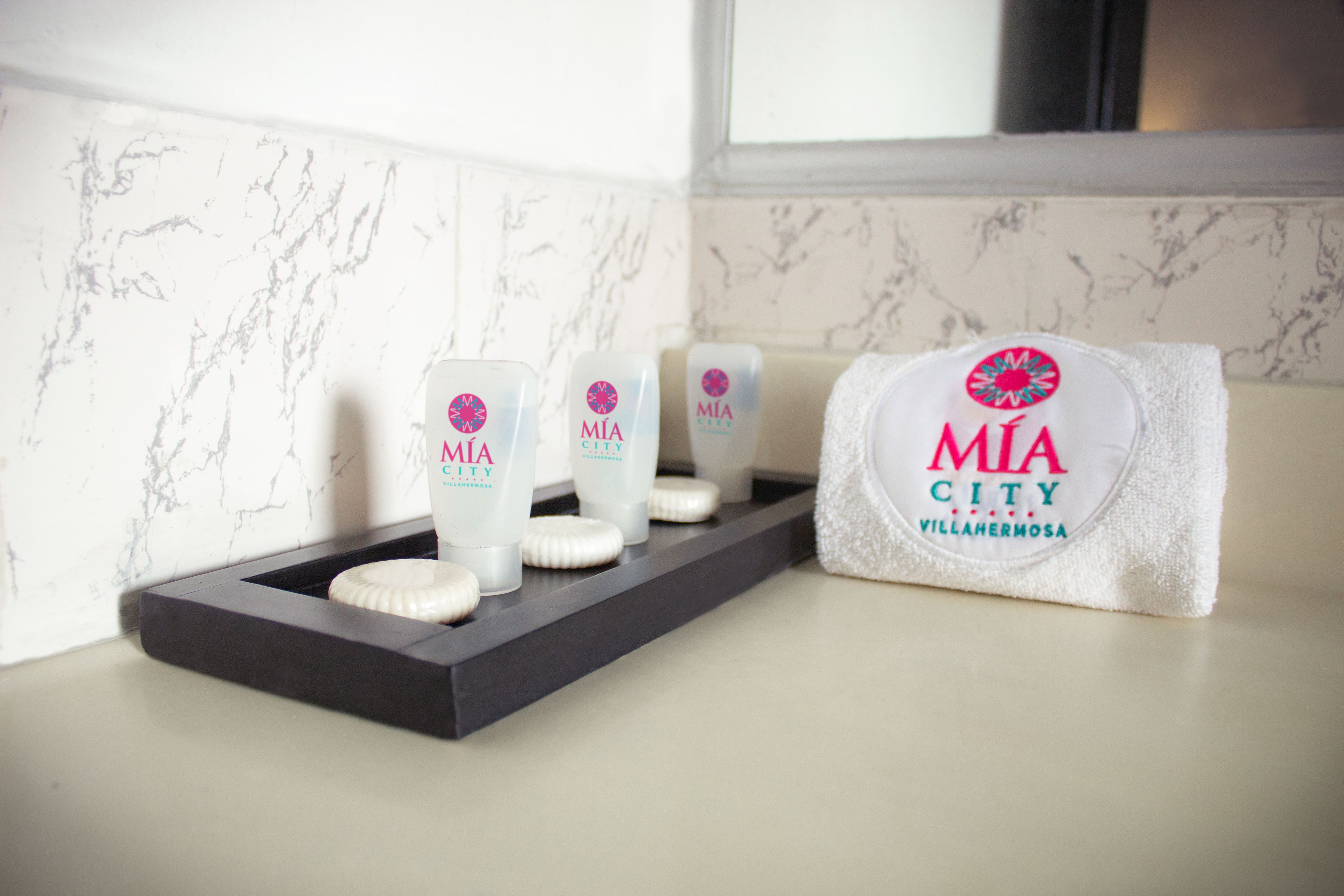 Uma bancada de banheiro com produtos de higiene pessoal e uma toalha com a marca "MIA CITY Villahermosa".