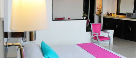 Une chambre d’hôtel comprenant un lit, une chaise, un bureau, une lampe et un coin cuisine.