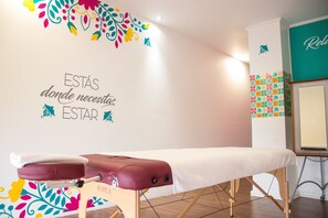 A massage table in a room with a decorative wall and a sign that reads "ESTAS donde necesitas ESTAR".