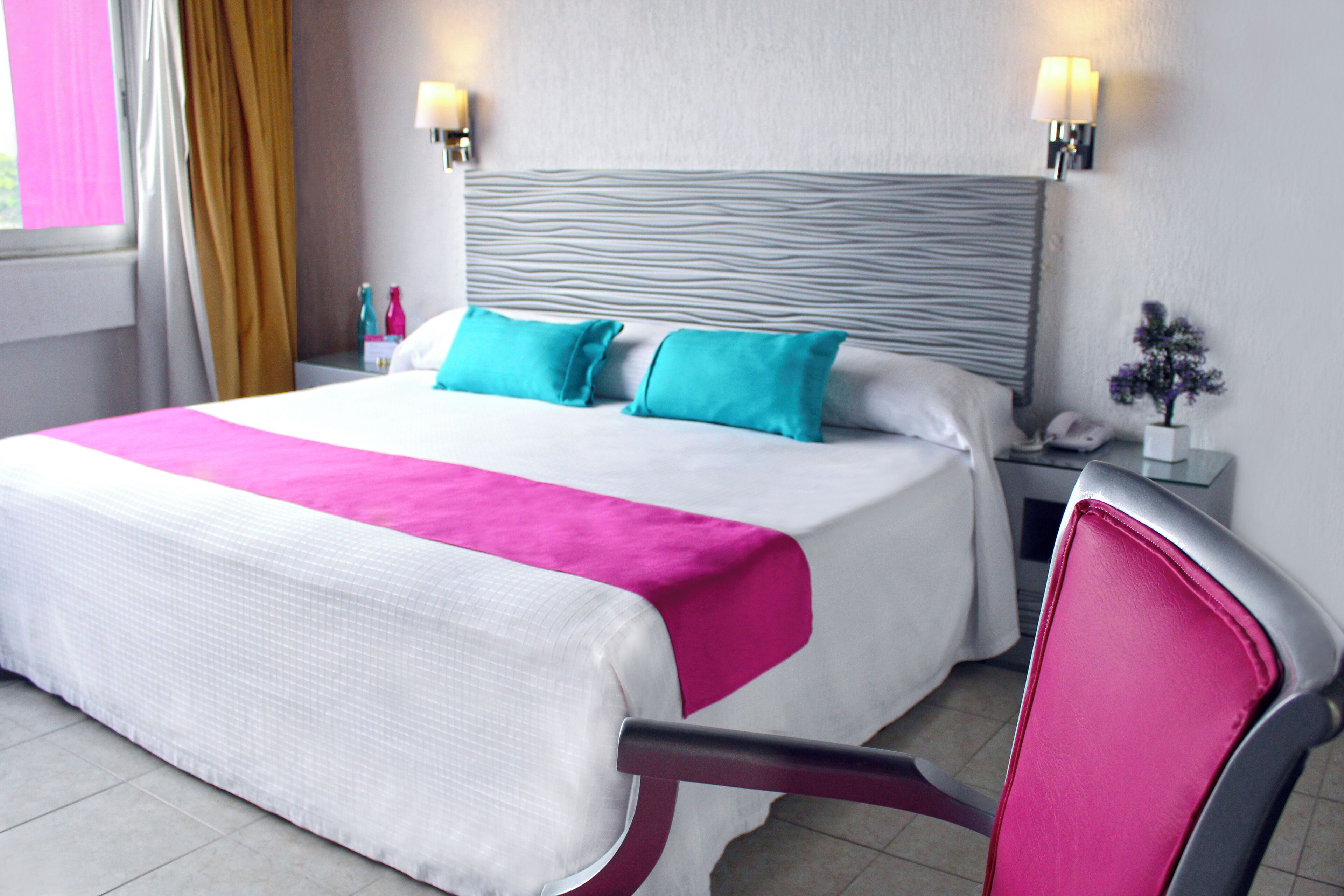 Una habitación de hotel con una cama, una silla, una mesita de noche y una lámpara.