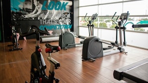 A gym with various exercise equipment, a large motivational poster, and a view of the city through large windows. - Mia City Villahermosa (Villahermosa)