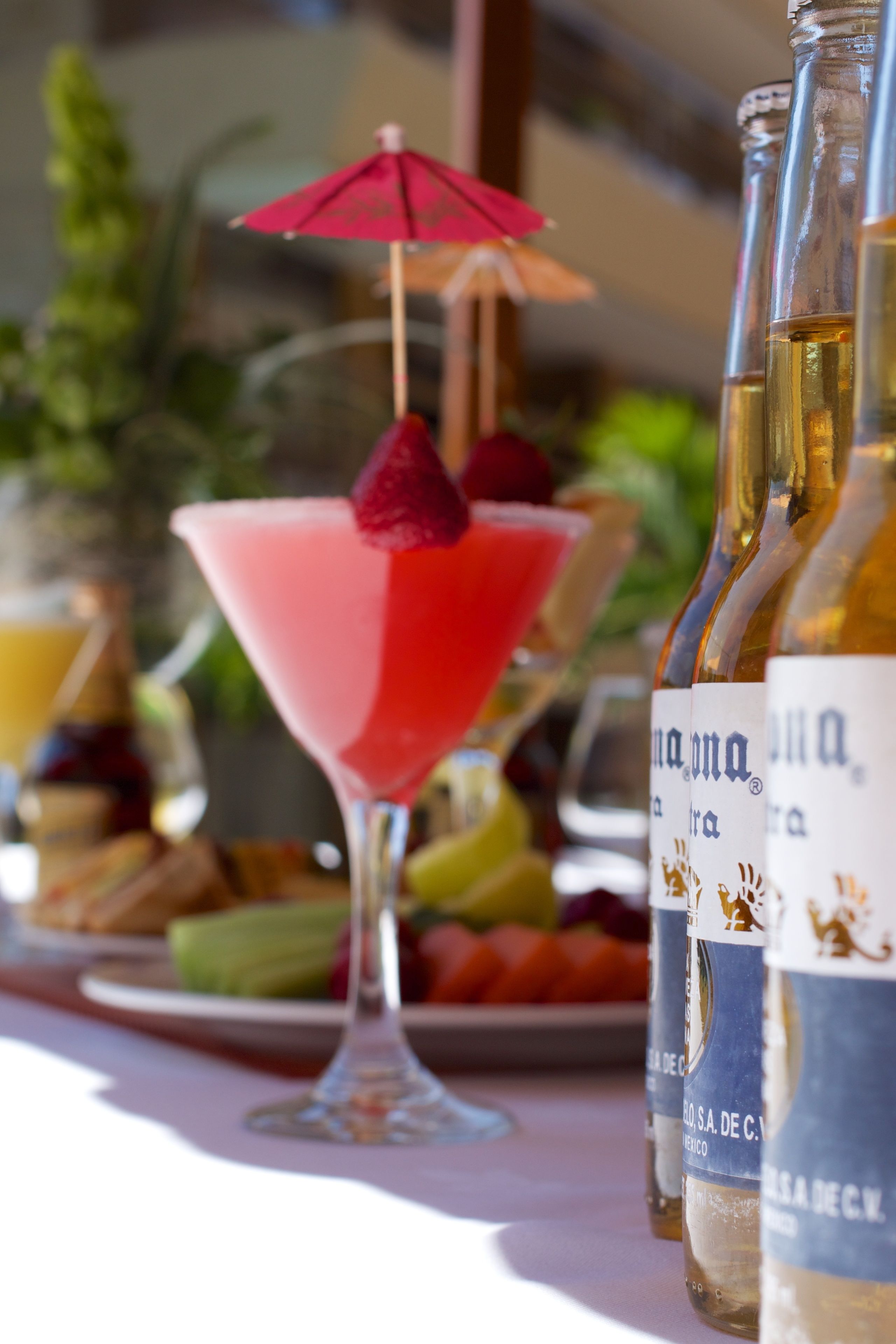 A table with a martini glass, a red umbrella, and bottles of a beverage.